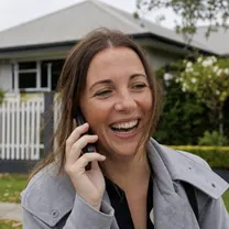 A property agent laughing on a phone call outside a house.