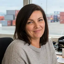 A freight forwarding estimator at her desk by the container yard, smiling.