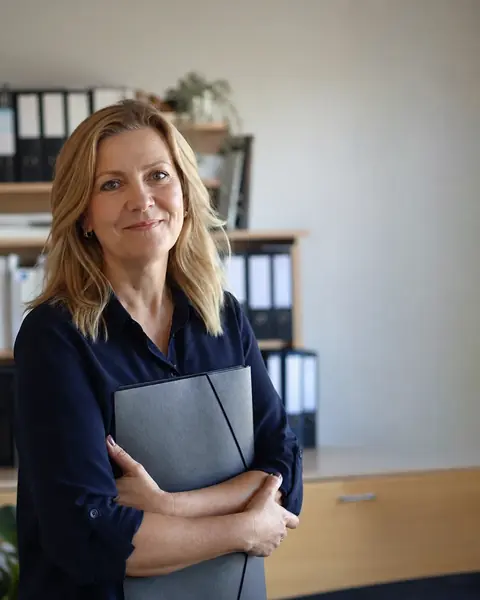 A bookkeeper in a tidy office, smiling, a folder under her arm.